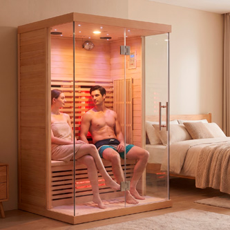 Couple sits inside a glass-front wooden sauna in a bedroom, wearing swimsuits and talking to each other.